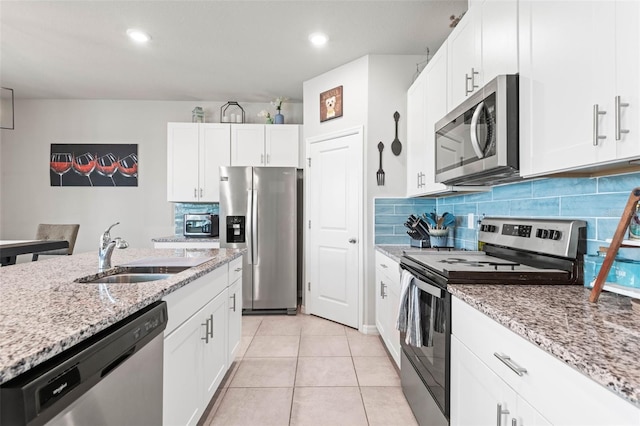 kitchen with light stone counters, light tile patterned floors, a sink, decorative backsplash, and appliances with stainless steel finishes