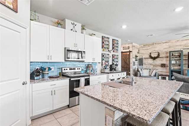 kitchen featuring a kitchen breakfast bar, stainless steel appliances, a barn door, white cabinets, and decorative backsplash