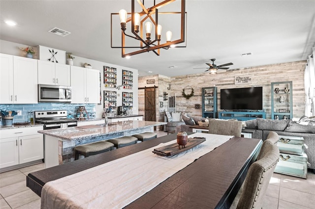 dining space featuring light tile patterned flooring, visible vents, a ceiling fan, and a barn door