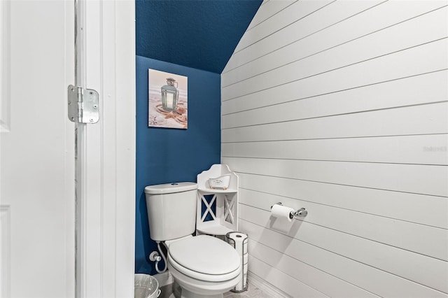 bathroom featuring wooden walls, toilet, and vaulted ceiling