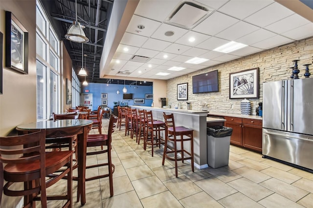 kitchen featuring a kitchen breakfast bar, high end refrigerator, a kitchen island, a paneled ceiling, and light tile patterned flooring