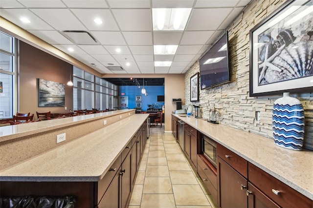 kitchen featuring sink, a drop ceiling, light stone counters, light tile patterned flooring, and hanging light fixtures