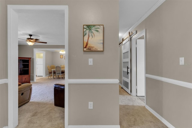 hall with crown molding, a barn door, baseboards, and light colored carpet