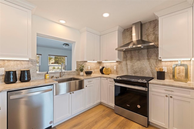 kitchen featuring stainless steel appliances, white cabinetry, a sink, and wall chimney exhaust hood