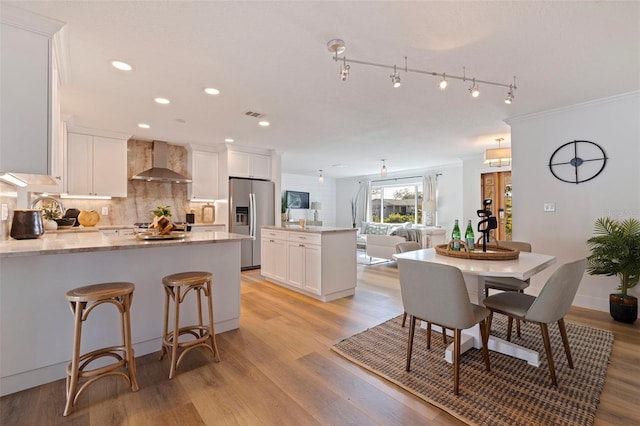 kitchen with a center island, wall chimney range hood, white cabinets, and stainless steel fridge