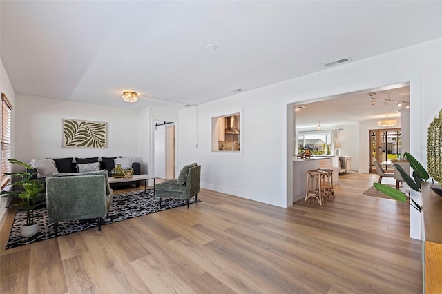 living area with baseboards, visible vents, light wood-style floors, and a barn door