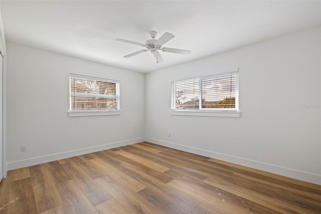 empty room featuring baseboards, a ceiling fan, wood finished floors, and plenty of natural light