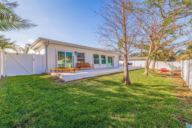 rear view of house featuring stucco siding, a patio area, a gate, a yard, and a fenced backyard