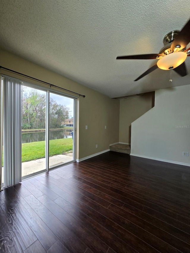 unfurnished living room featuring dark wood-style flooring, a water view, a ceiling fan, a textured ceiling, and baseboards