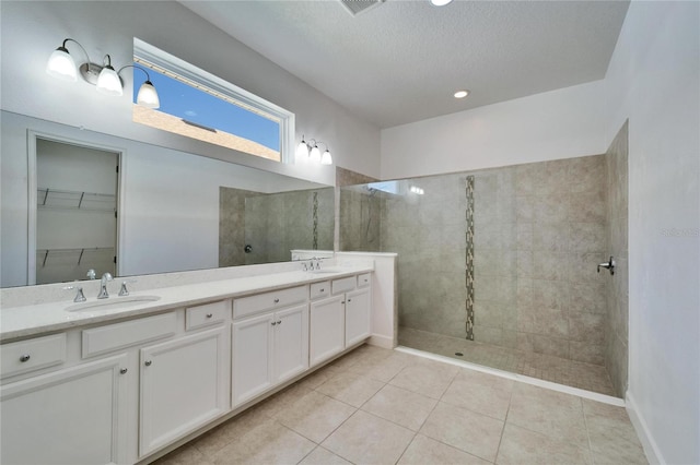 bathroom with tile patterned floors, tiled shower, a textured ceiling, and vanity