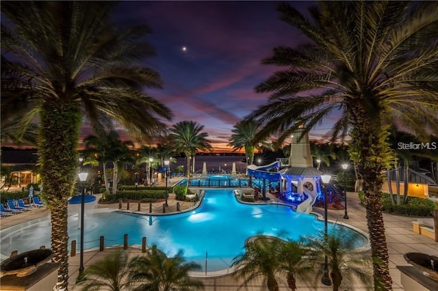 pool at dusk featuring a patio and a water slide