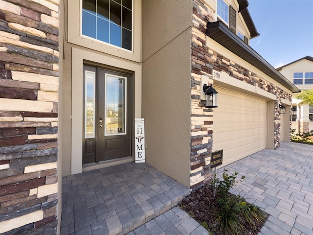 doorway to property with a garage, stone siding, decorative driveway, and stucco siding