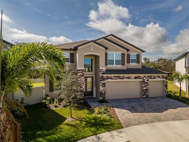 view of front of home with fence, stone siding, decorative driveway, stucco siding, and a front lawn