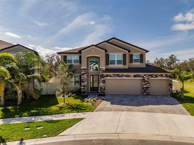 view of front of property with decorative driveway, stucco siding, an attached garage, a front yard, and stone siding