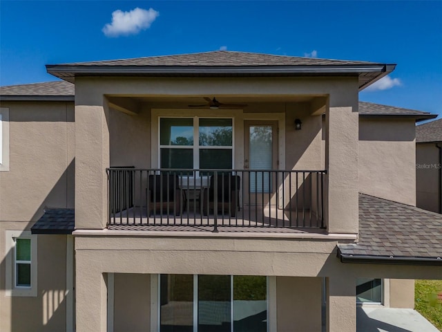 rear view of house featuring roof with shingles, a balcony, and stucco siding