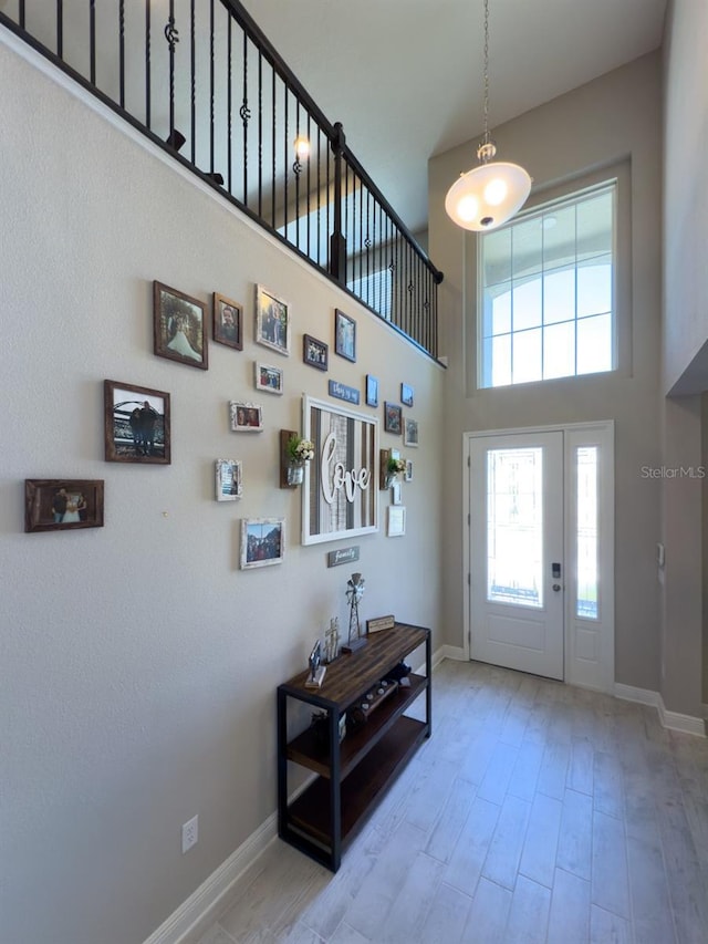 entryway with a towering ceiling, baseboards, and light wood finished floors