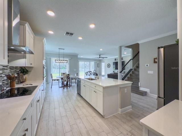 kitchen with a kitchen island with sink, visible vents, light countertops, and wall chimney range hood
