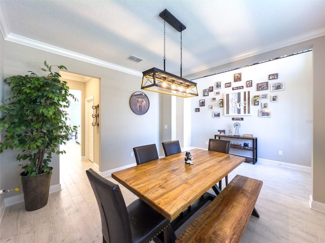 dining space featuring baseboards, light wood-style flooring, visible vents, and crown molding