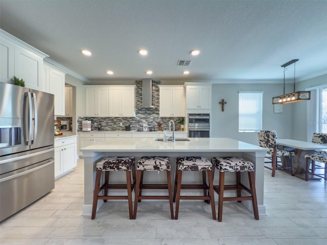 kitchen with a center island with sink, stainless steel appliances, light countertops, visible vents, and wall chimney exhaust hood