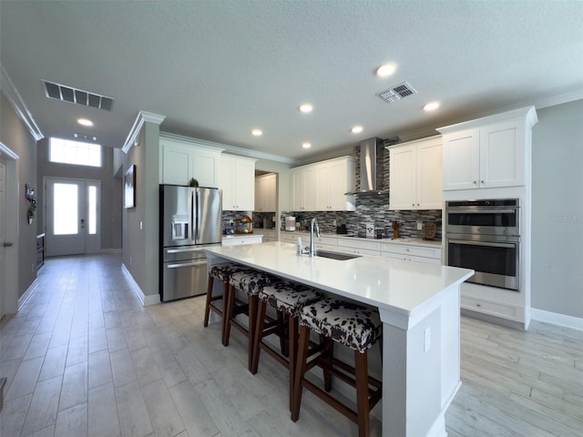 kitchen featuring visible vents, wall chimney exhaust hood, stainless steel appliances, light countertops, and a sink