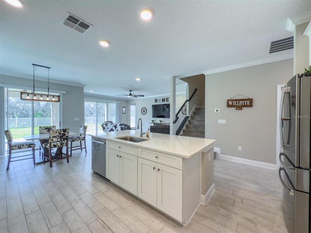 kitchen featuring a sink, light countertops, appliances with stainless steel finishes, an island with sink, and decorative light fixtures
