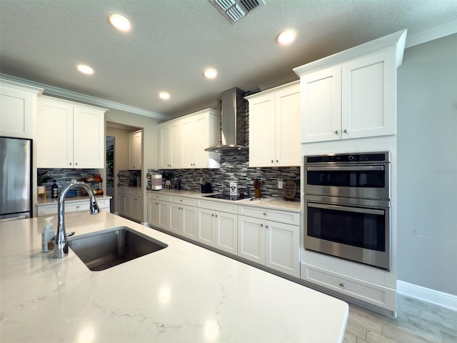 kitchen with a sink, visible vents, white cabinetry, appliances with stainless steel finishes, and wall chimney exhaust hood