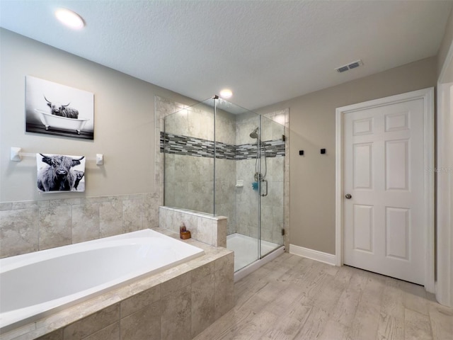 full bathroom featuring a textured ceiling, a garden tub, wood finished floors, visible vents, and a shower stall