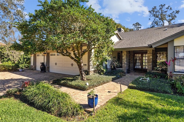 view of front of property with a shingled roof, an attached garage, decorative driveway, french doors, and a front lawn