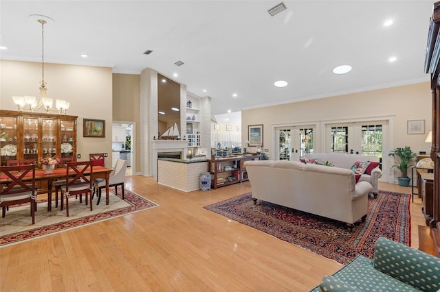 living room with crown molding, french doors, light wood-style floors, a fireplace, and a notable chandelier