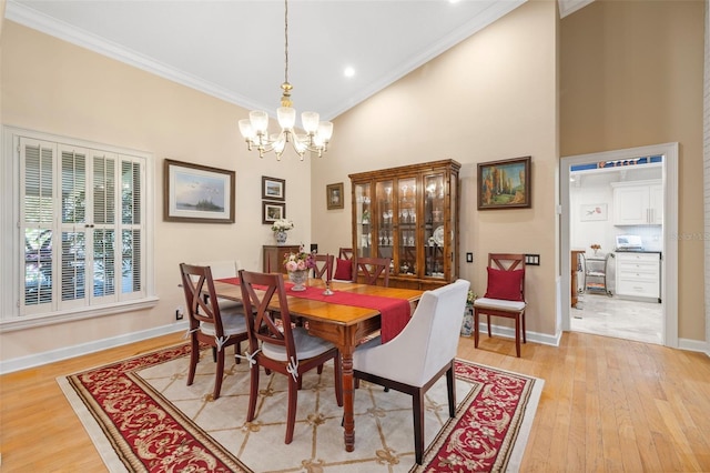 dining area featuring baseboards, a towering ceiling, ornamental molding, light wood-style floors, and a chandelier