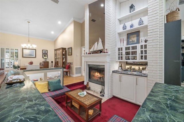 living room with visible vents, a fireplace with flush hearth, ornamental molding, an inviting chandelier, and high vaulted ceiling