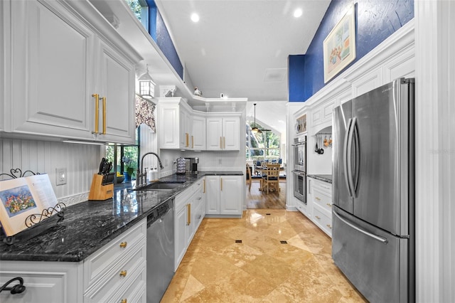 kitchen featuring stainless steel appliances, white cabinets, a sink, and dark stone countertops