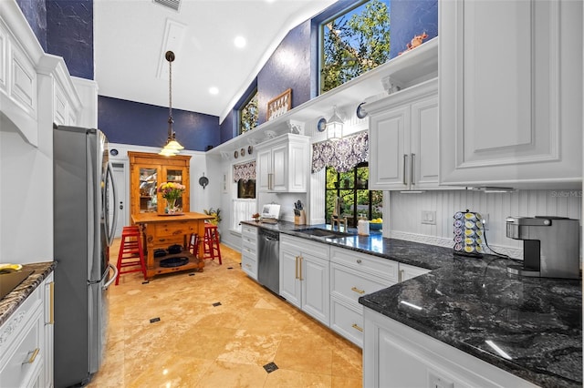 kitchen featuring white cabinets, dark stone counters, appliances with stainless steel finishes, high vaulted ceiling, and pendant lighting