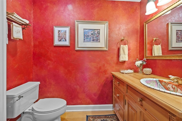 half bath with baseboards, vanity, toilet, and wood finished floors