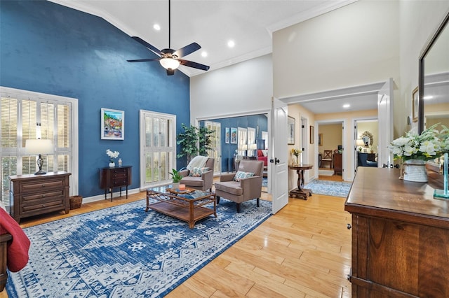 living room with baseboards, ceiling fan, crown molding, light wood-style floors, and high vaulted ceiling