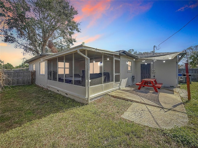 back house at dusk featuring a patio area, a lawn, and a sunroom