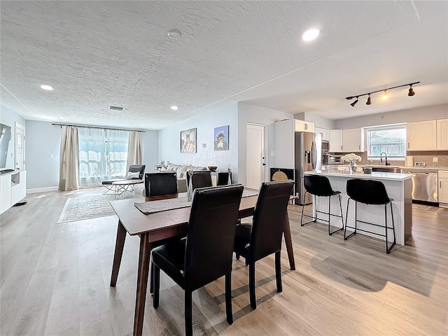 dining room featuring rail lighting, light hardwood / wood-style flooring, sink, and a textured ceiling