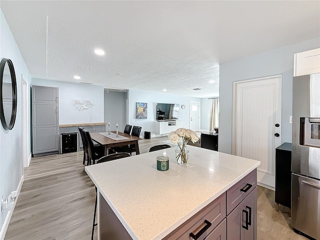 kitchen featuring a center island, a textured ceiling, stainless steel fridge with ice dispenser, light hardwood / wood-style floors, and light stone countertops