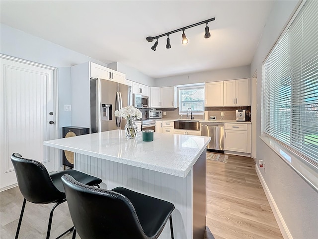 kitchen with appliances with stainless steel finishes, sink, light stone counters, a kitchen island, and white cabinets