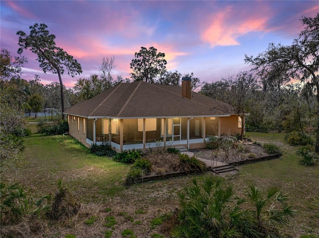 back house at dusk featuring a lawn