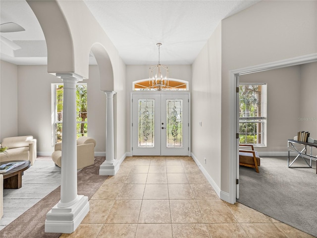 foyer with a notable chandelier, french doors, decorative columns, and light carpet