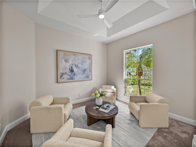 carpeted living room with ceiling fan and a raised ceiling