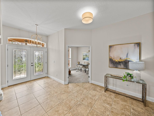 entrance foyer featuring light tile patterned flooring, an inviting chandelier, french doors, and a textured ceiling