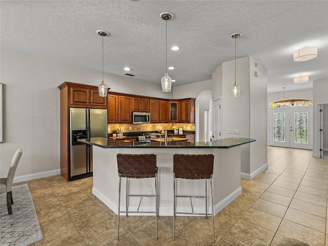 kitchen with a breakfast bar area, stainless steel appliances, an island with sink, french doors, and decorative light fixtures