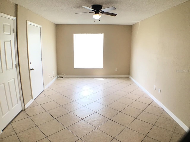 unfurnished room with light tile patterned floors, ceiling fan, baseboards, and a textured ceiling