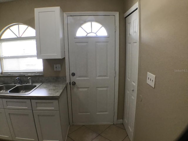 kitchen with dark countertops, white cabinets, a sink, and light tile patterned flooring