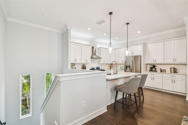 kitchen with sink, stainless steel refrigerator with ice dispenser, white cabinetry, wall chimney exhaust hood, and hanging light fixtures