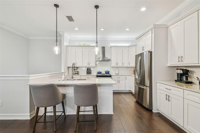 kitchen featuring white cabinets, pendant lighting, stainless steel appliances, and wall chimney exhaust hood