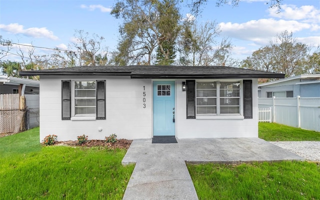 view of front facade featuring concrete block siding, fence, and a front yard