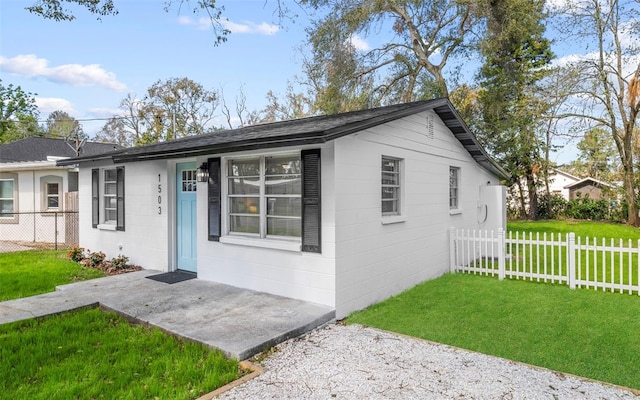 view of front of home with fence, a front yard, a patio, and concrete block siding